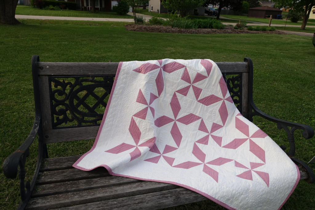 A White Quilt with a Pink Border and Pinwheels Assembled from a Pre-cut Quilt Kit